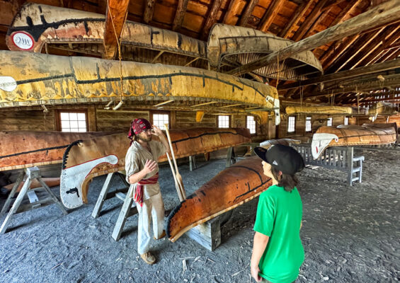 19th century canoe builder in Fort William, a living history site giving an overview of the craft to a boy.